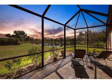 Screened patio featuring brick flooring with outdoor furniture and peaceful lake views at sunset at 2104 Batello Dr, Venice, FL 34292