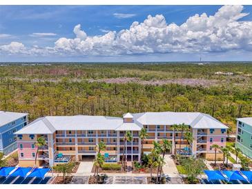 Multi-level condo building featuring colorful facade, covered parking, and tropical landscaping against a scenic natural backdrop at 8409 Placida Rd # 206, Placida, FL 33946