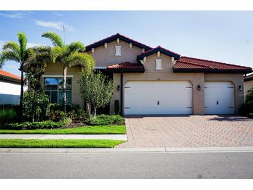 Charming single-story home boasts a red tile roof, two-car garage, paver driveway, and lush landscaping at 136 Positano Trl, Nokomis, FL 34275