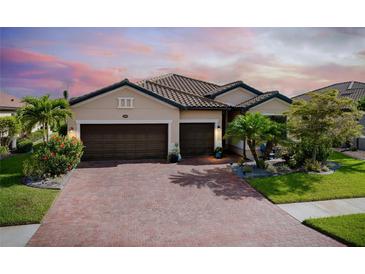 Charming single-story home boasts a three-car garage, tiled roof, brick driveway, and lush landscaping at 13634 Vancanza Dr, Venice, FL 34293