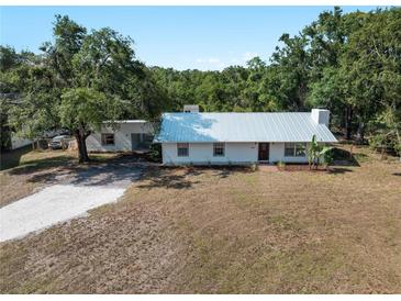 Charming single-story home with a white metal roof, surrounded by mature trees and a gravel driveway at 2008 55Th E Ave, Bradenton, FL 34203