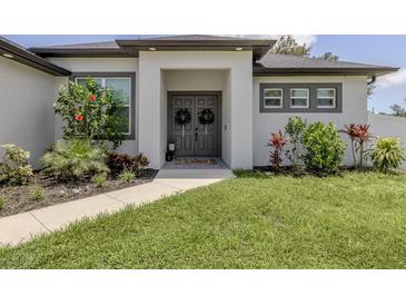 Charming home featuring a covered entry with double doors, manicured landscaping, and a well-maintained lawn at 2245 Pickard Ln, North Port, FL 34286