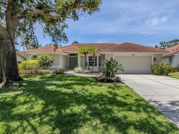 Charming single-story home with a well-manicured lawn and a tile roof, complemented by mature trees and lush landscaping at 609 Madrid Ave, Venice, FL 34285
