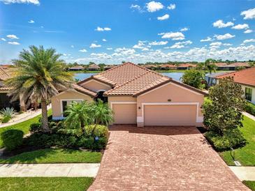 Charming single-Gathering home featuring a brick driveway, well-manicured lawn, and tropical landscaping by the lake at 20370 Grazie Pl, Venice, FL 34293