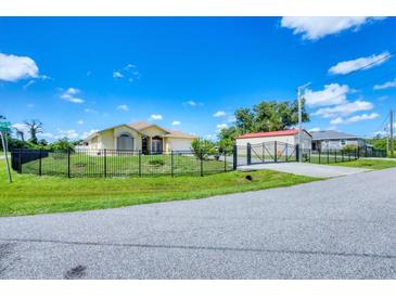 Charming yellow house with a gated entrance, lush lawn, and a clear blue sky at 102 Bayamo Dr, North Port, FL 34287