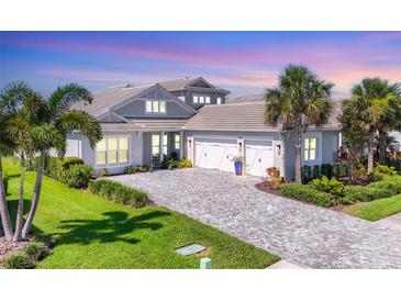 Beautiful gray home featuring a three-car garage, lush landscaping, and a paver driveway at 8245 Grande Shores Dr, Sarasota, FL 34240