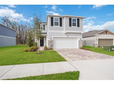 Two-story home featuring a two-car garage, paver driveway, stone accents, and manicured lawn at 37545 Mackenzie Dr, Zephyrhills, FL 33540
