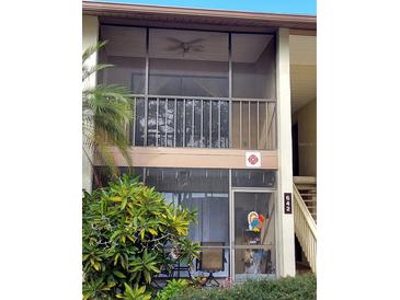 View of the home's exterior featuring a screened balcony with outdoor seating, with green foliage visible at 642 Bird Bay E Dr # 205, Venice, FL 34285
