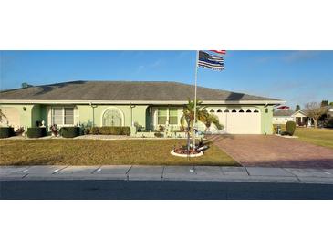Charming one-story home with a green facade, mature landscaping, and a brick-paved driveway at 906 Bluewater Dr, Sun City Center, FL 33573