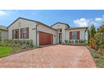 Beautiful single-story home with a red brick driveway, wood shutters, and a two-car garage at 14517 Coastal Woodland Ln, Parrish, FL 34219