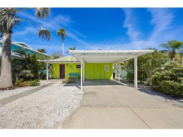 Charming home featuring a covered carport, vibrant colors, and tropical landscaping at 318 182Nd E Ave, Redington Shores, FL 33708