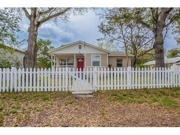 Charming single-story home featuring a red door, a white picket fence, and mature trees in the front yard at 3408 Phillips St, Tampa, FL 33619