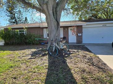 Charming brick home featuring a mature tree, tire swing and a white bicycle at 4706 Lansing Ne St, St Petersburg, FL 33703