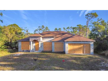 Exterior view of a single-story house with boarded up windows and an unfinished entrance, set on a grassy lot at 6098 San Salvador Rd, North Port, FL 34291