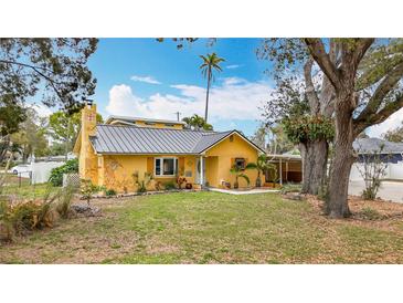 Charming yellow home featuring a metal roof, well-manicured lawn, and beautiful landscaping at 8135 33Rd Ave N, St Petersburg, FL 33710