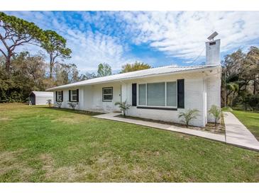 Inviting home featuring a white brick exterior, metal roof, and lush green lawn at 18526 Sweetbay Ln, Dade City, FL 33523