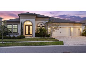 Elegant home featuring a three-car garage, arched entry, and manicured landscaping at 5516 Madrigal Way, Apollo Beach, FL 33572