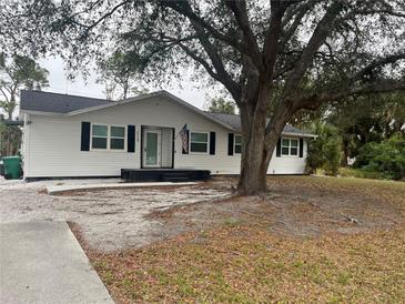 Charming one-story white home featuring black shutters, an American flag, and mature trees at 15168 Chamberlain Blvd, Port Charlotte, FL 33953