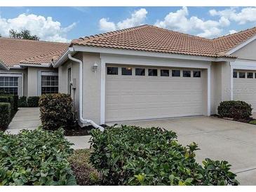 Beige house featuring a two-car garage with a tile roof and manicured landscaping at 1830 San Silvestro Dr, Venice, FL 34285