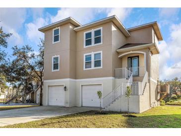Two-story beige home featuring white trim, multi-car garage, and staircase leading to the front door at 7327 Brightwaters Ct, New Port Richey, FL 34652