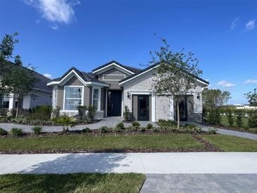 Charming single-story home featuring stone accents, gray siding, manicured landscaping, and a welcoming entrance at 2718 Wise River Lane, Zephyrhills, FL 33539