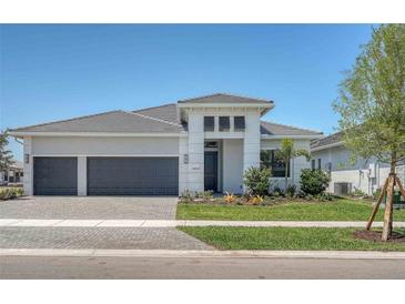 A modern, light gray, single-story home with a three-car garage and manicured landscaping under a clear, blue sky at 18213 Cresswind Ter, Lakewood Ranch, FL 34211