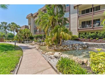 Beautiful condo exterior featuring a lushly landscaped water feature with palm trees and a sidewalk on a sunny day at 3035 Countryside Blvd # 15B, Clearwater, FL 33761