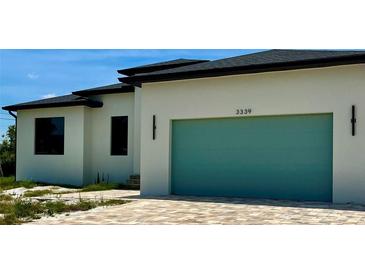 Modern home featuring a teal garage door, light stucco and a patterned brick driveway at 3339 Elkcam Blvd, Port Charlotte, FL 33952
