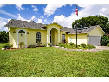 Charming yellow home with manicured lawn, arched entryway, and American flag at 9475 Dunkirk Rd, Spring Hill, FL 34608