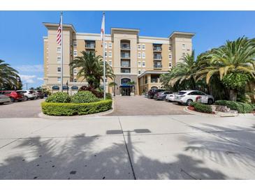 Beautiful tan apartment building featuring lush landscaping, palm trees, and prominent American flags at 1064 N Tamiami Trl # 1219, Sarasota, FL 34236