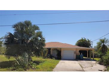 A single-Gathering home featuring a tan exterior, attached garage, and a lush front yard with mature palm trees at 155 Summerset Dr, Punta Gorda, FL 33982