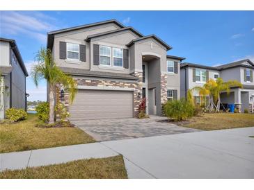 Beautiful two story home featuring a two car garage, stone accents, manicured lawn, and lush palm trees at 3137 Marine Grass Dr, Wimauma, FL 33598