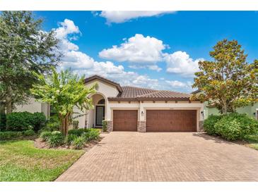Charming home featuring a barrel tile roof, well-manicured landscaping, and a brick paver driveway leading to a three-car garage at 12784 Burns Dr, Odessa, FL 33556