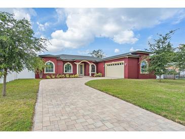 Elegant red home featuring a paver driveway, lush lawn, arched windows, and an attached two-car garage at 3244 55Th Ave N, St Petersburg, FL 33714