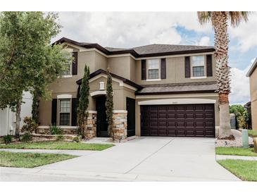 Two-story tan house with brown trim, stone accents, a dark brown garage door, and beautiful landscaping at 9221 Mountain Magnolia Dr, Riverview, FL 33578