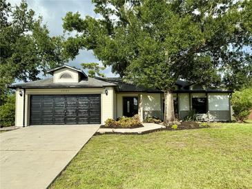 Charming single-story home featuring a black garage door, well-maintained lawn, and mature landscaping at 19543 Midway Blvd, Port Charlotte, FL 33948