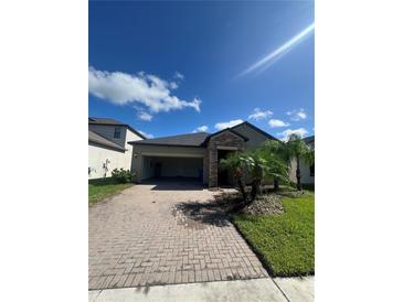 Charming single-Gathering home with stone accents, a brick driveway, and tropical landscaping at 13244 Satin Lily Dr, Riverview, FL 33579