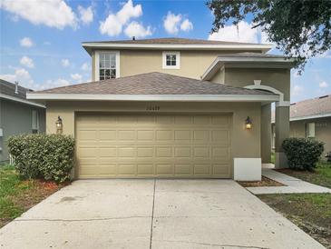 Beige two-story home featuring an attached two-car garage and manicured front bushes under a cloudy blue sky at 10429 Avelar Ridge Dr, Riverview, FL 33578