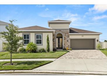 Beautiful single-story home featuring manicured lawn, stone accents and a brick paved driveway leading to a two-car garage at 8297 Ivy Stark Blvd, Wesley Chapel, FL 33545