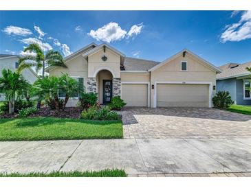 Two-story house with beige exterior, three car garage, and landscaped yard at 5330 Silver Sun Dr, Apollo Beach, FL 33572