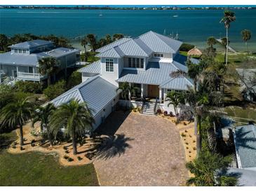 Stunning waterfront home featuring lush landscaping, a gray metal roof, and a brick paver driveway at 764 S Mccall Rd, Englewood, FL 34223
