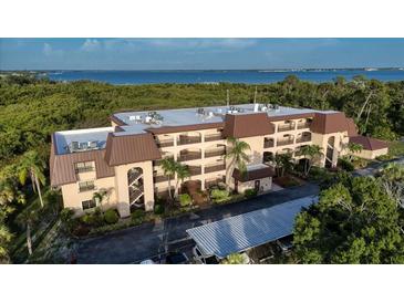 Coastal condo building with balconies, mature landscaping, and covered parking near the water at 23465 Harborview Rd # 223, Punta Gorda, FL 33980