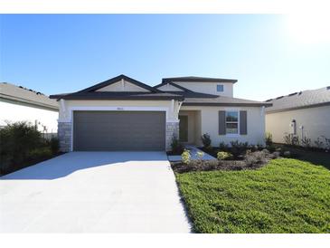 Charming single-story home featuring a manicured lawn, neutral paint, and a two-car garage with stone accents at 9868 Last Light Gln, Parrish, FL 34219