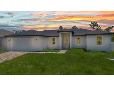 Charming single-story home with a brick driveway and lush green lawn at sunset at 8489 Topeka Cir, Port Charlotte, FL 33981