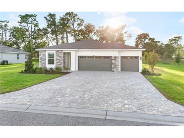 Beautiful single-story home with a gray brick driveway, stone accents, manicured lawn, and a two-car garage at 9127 Players Dr, Weeki Wachee, FL 34613