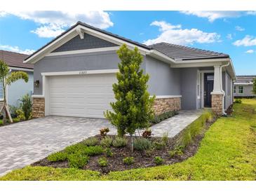 Exterior view of a single-story home with a gray exterior, white garage door and landscaping at 11223 Livewell Ct, Venice, FL 34293