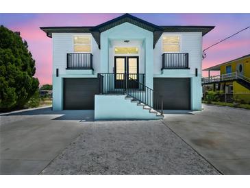 Charming two-story home featuring a unique aqua and white color scheme, double garages, and elevated entry with black railings at 3230 Azalea Drive # Lot 13, Hernando Beach, FL 34607
