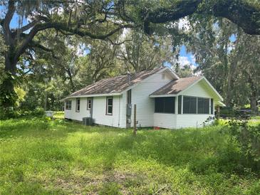 White house exterior with screened porch, surrounded by lush green grass and mature trees at 1205 S Main St, Brooksville, FL 34601
