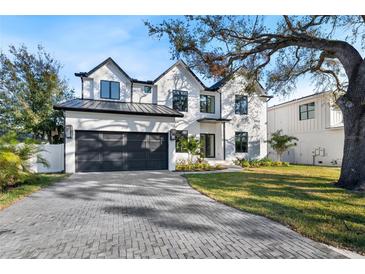 Stunning new construction home featuring a brick driveway, lush lawn, and a dark colored, three-car garage at 2106 S Cortez Ave, Tampa, FL 33629