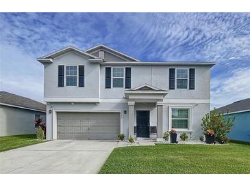 Two-story house with gray siding, gray garage door, and landscaping at 17206 White Mangrove Dr, Wimauma, FL 33598